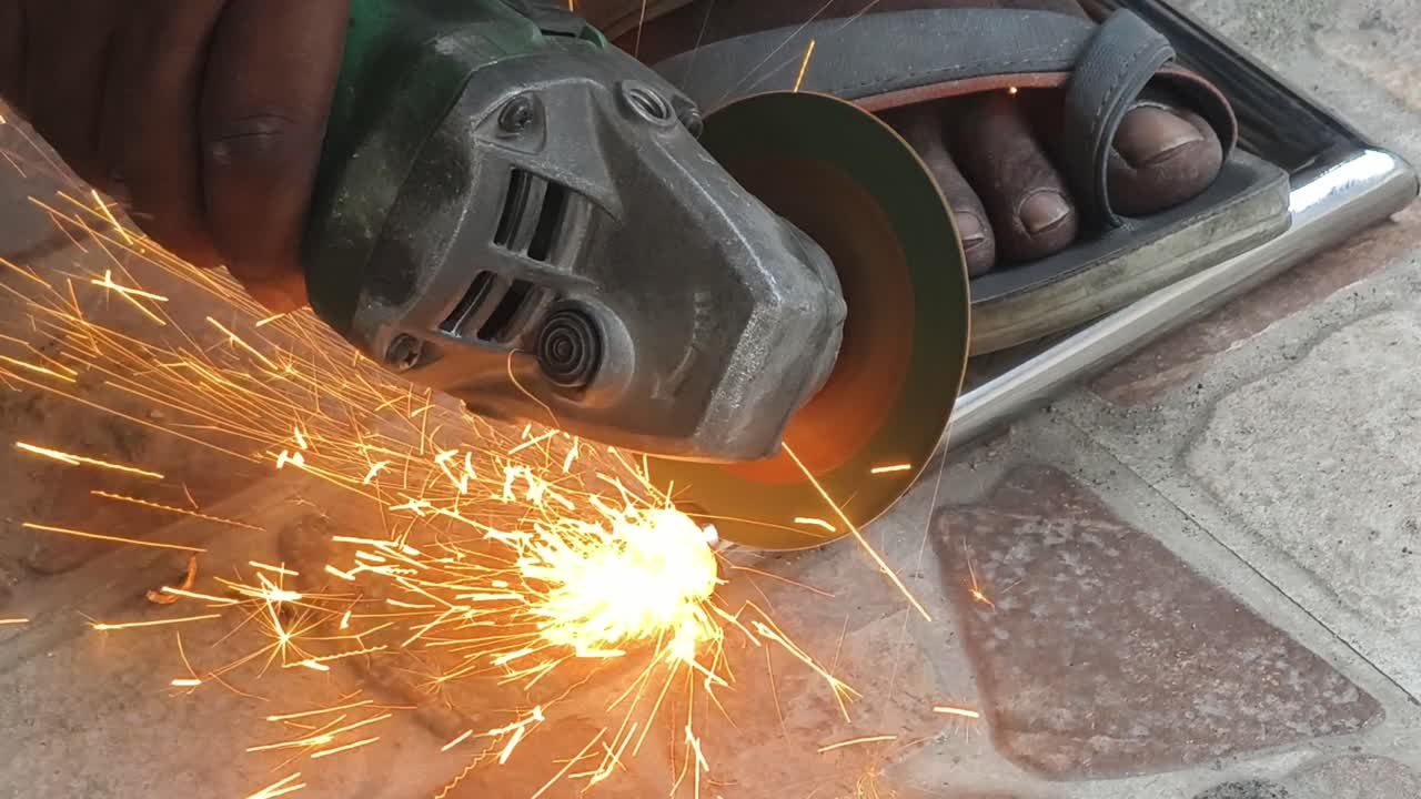 Close-up da mão de um trabalhador indiano usando uma ferramenta elétrica para cortar um tubo de metal, criando faíscas laranja brilhantes. Ideal para conteúdo de construção, faça você mesmo e segurança industrial.