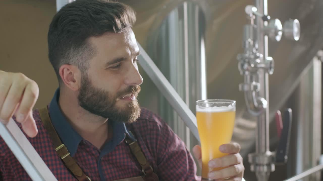 un joven cervecero con un delantal de cuero está probando cerveza en una cervecería moderna
