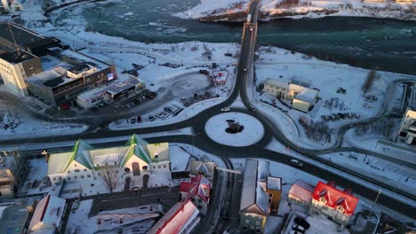 vehicles driving at roundabout in the selfoss town at sunset during winter in south iceland. aerial tilt-up shot