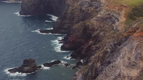 steep eroded escarpment cliffs drop off into black sand beach on north shore of west maui