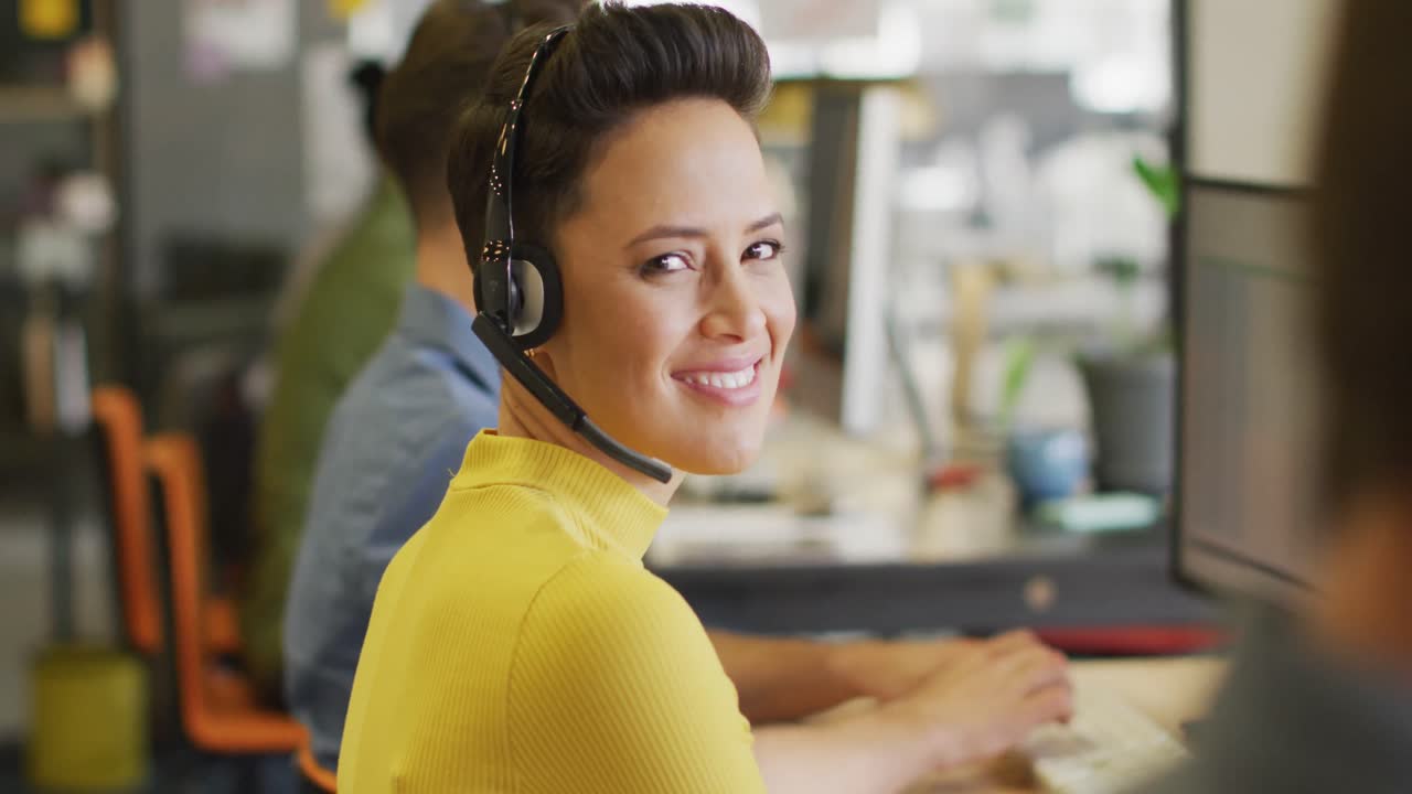 Portrett av glad kaukasisk forretningskvinne som bruker telefonhodesett og ser på kameraet på kontoret.