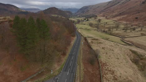rising above lakeland road with single car.. revealing wider mountainous landscape and lake. lake district, cumbria, uk.