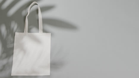 leaf shadow moving over white bag on grey background, copy space, slow motion