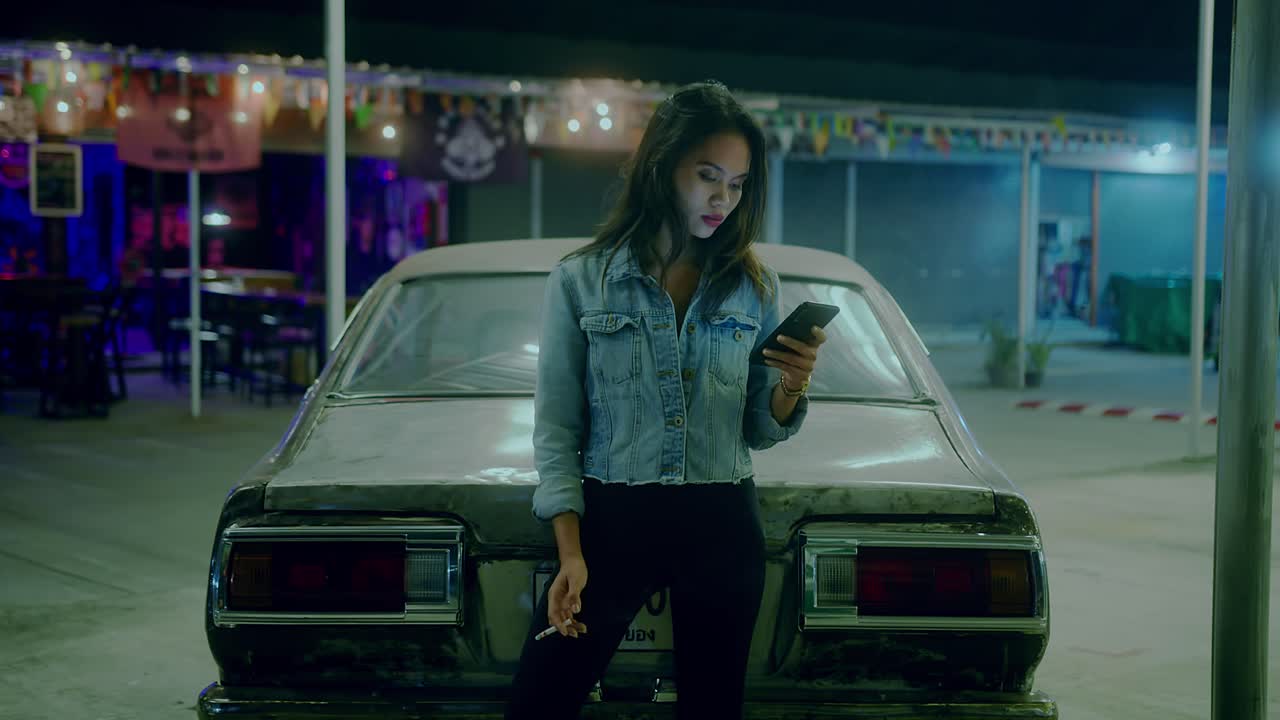 Donna con telefono vicino a un'auto d'epoca di notte