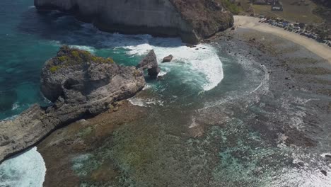 vista aérea de la playa de atuh en nusa penida, indonesia en un día soleado y con agua azul cristalina golpeando las formaciones rocosas