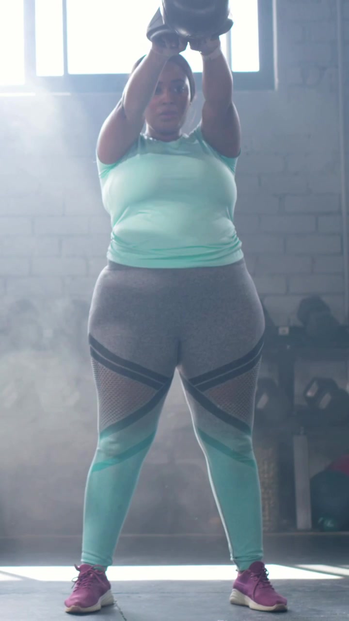 Donna adulta che esegue uno squat con kettlebell sopra la testa, iniziando un'oscillazione dalla posizione sumo per il fitness