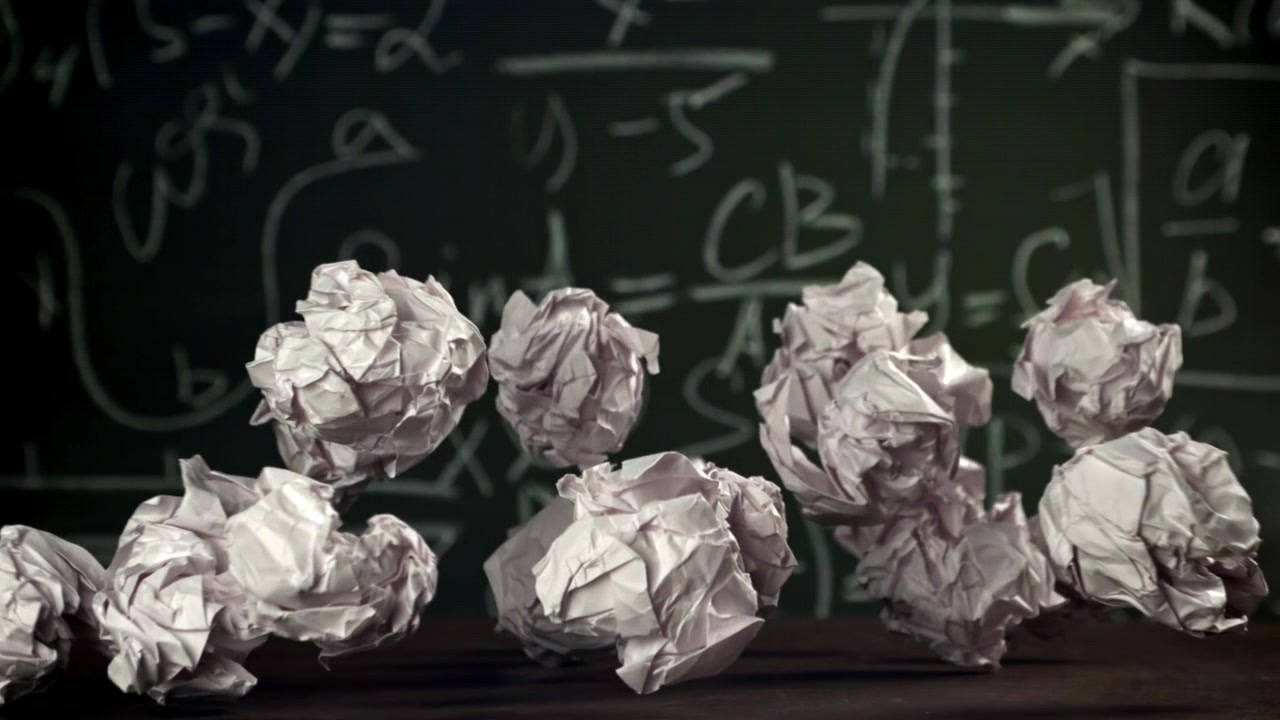 Crumpled Paper Balls Falling in Slow Motion Against a Chalkboard
