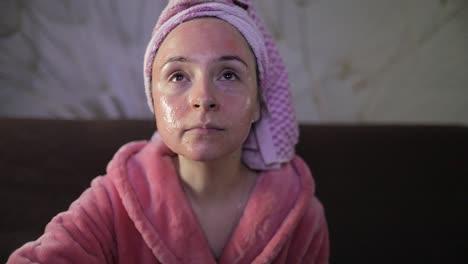 Mujer-Viendo-Una-Película-Nocturna-En-La-Televisión,-Comiendo-Palomitas-De-Maíz.-Bata-De-Baño,-Mascarilla-Facial