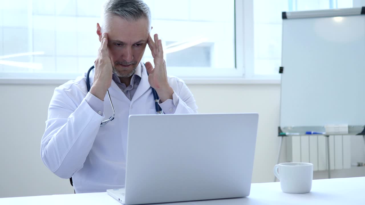 Mal di testa, medico stanco che lavora al portatile