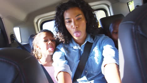 young black mother taking photos with two children in a car