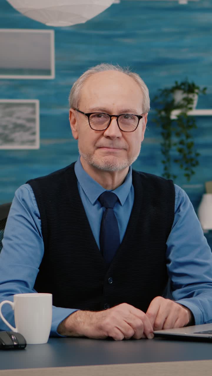 Vertical video: Elderly businessman entrepreneur sitting in workspace looking at camera