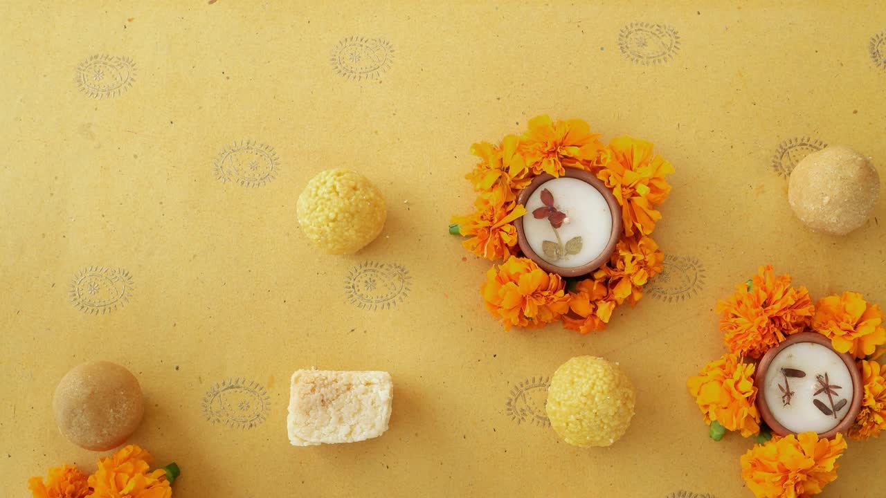 Human hand takes and then puts the last sweets along with flowers, diyas on a Indian background for Hindu festival of lights, Dusshera and Diwali preparation and celebration ingredients