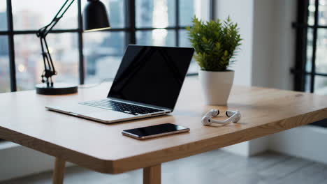 a modern, minimalist workspace with a laptop, phone, and plant on a wooden desk