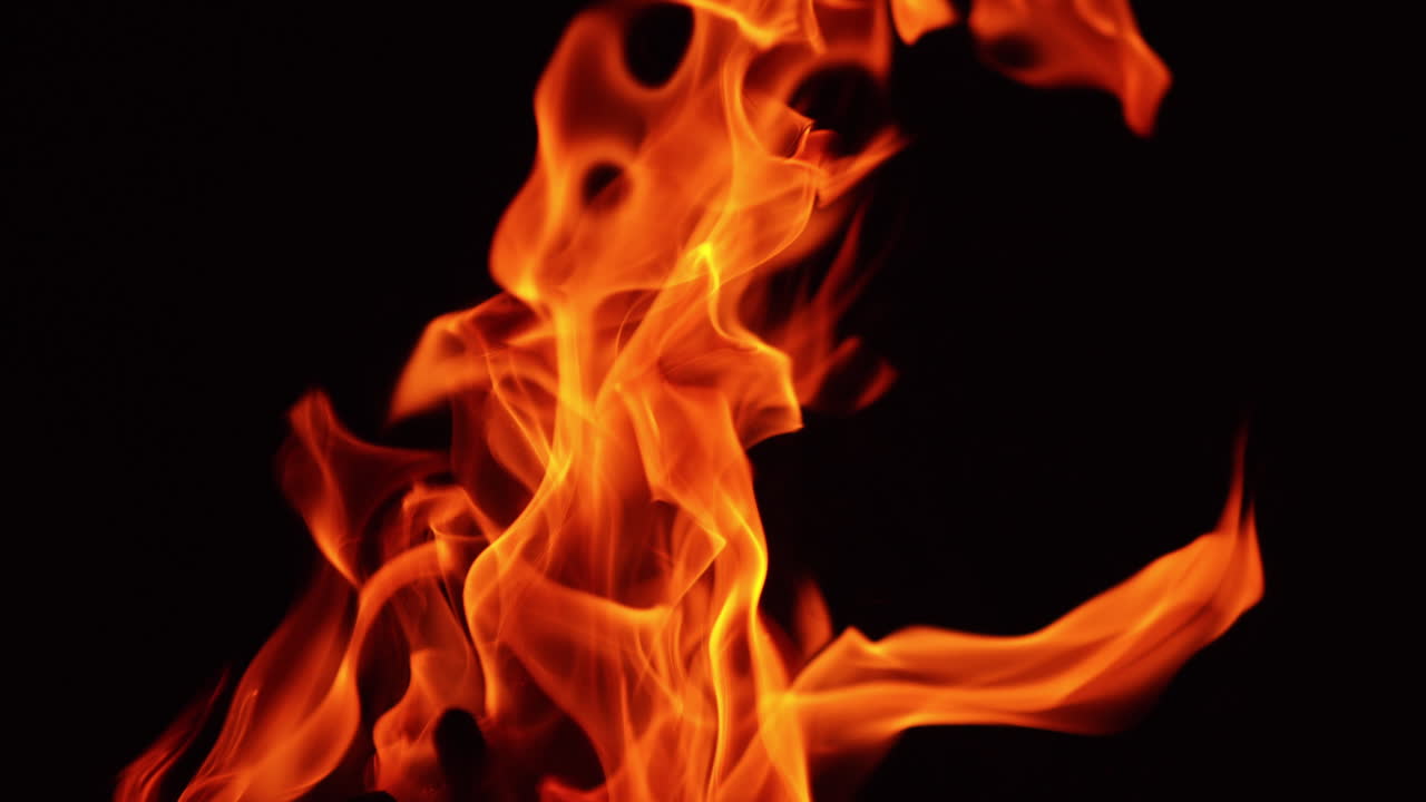 Bright flame rising up in the darkness. Tongues of bonfire moving in the wind at night. Close up.