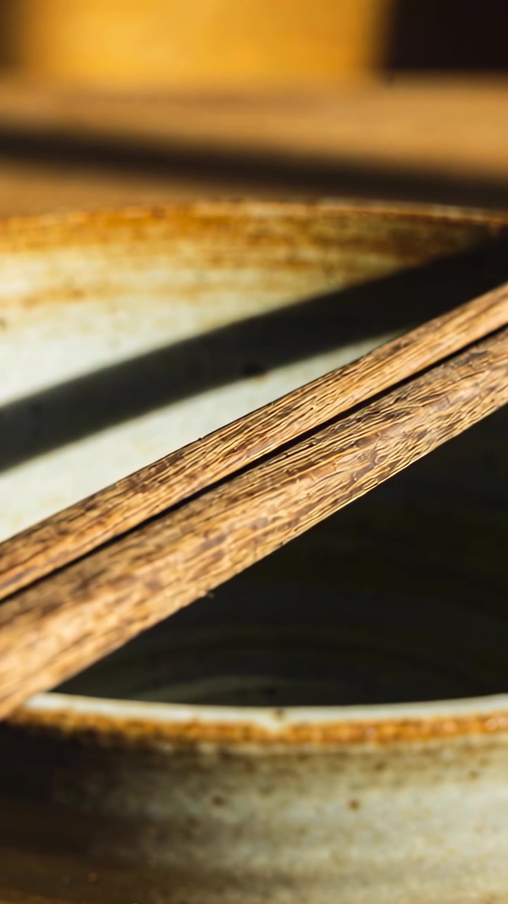 Video verticale: Telecamera in movimento, bacchette di legno che mettono a fuoco in cucina sul bordo di una ciotola, brodo scuro.
