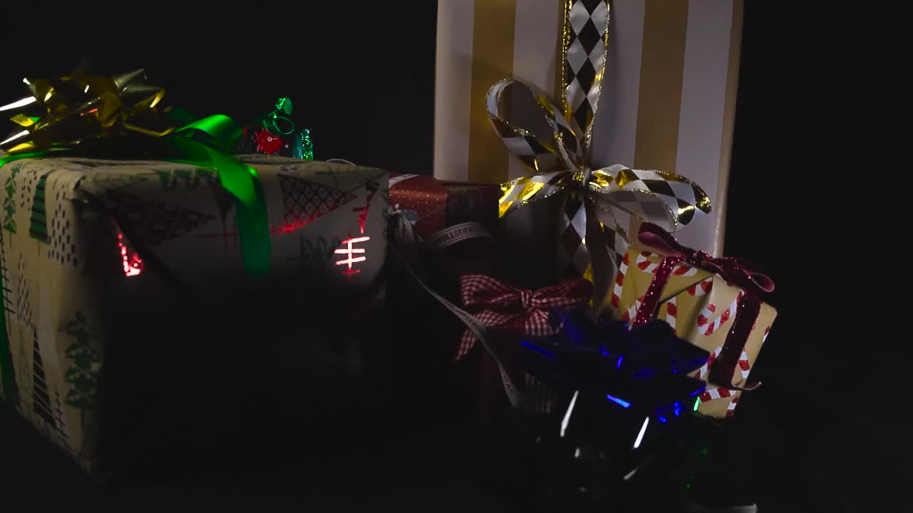 Close up view of colorful and shiny gift bows falling on Christmas presents or holiday gifts in slow motion in front of black studio background. Shallow depth of field. Colorful ribbons and wrappings