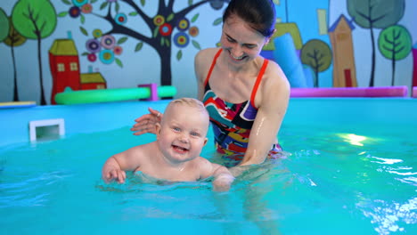 happy little baby boy learning to swim in the swimming pool. female coach supports a cute lovely kid.