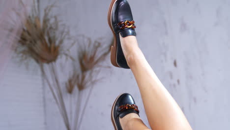 caucasian female model's legs lifted up to demonstrate footwear. stylish black shoes on tractor soles with chain décor close up.