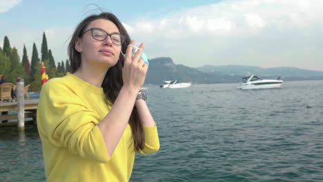 Slow-motion-shot-of-young,-beautiful-woman-with-glasses-removing-her-protective-mask,-scenic-landscape