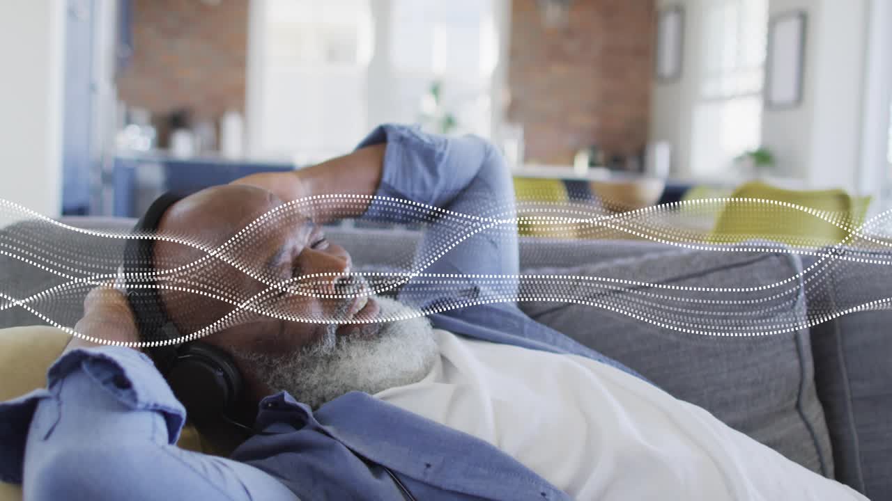 Senior man lounging on sofa, moving to music and adjusting headset as dotted waveform sweeping over