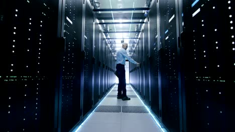 server engineer in data center walks through sliding doors and opens server rack cabinet.