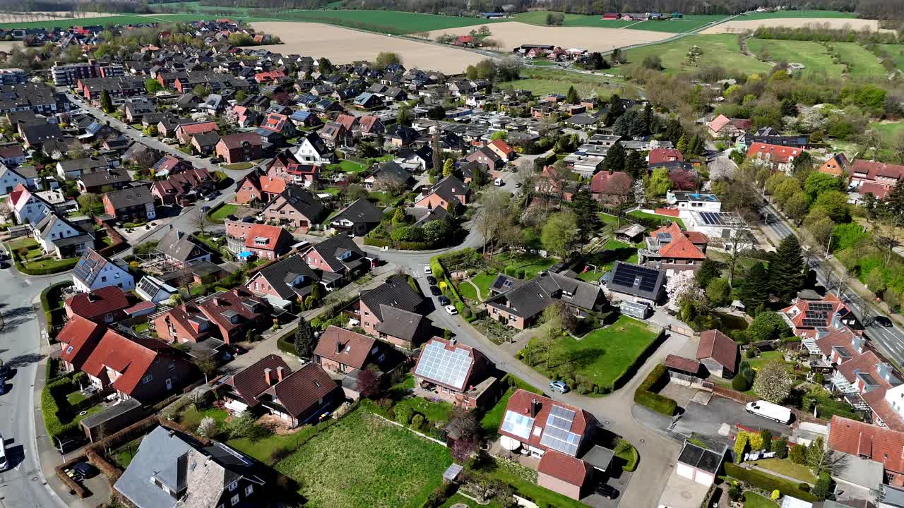 Solpaneler på taget af enfamiliehuse i et amerikansk boligområde. Solrig dag med grønt græs og landbrugsmarker i det fjerne. Bredt luftfoto fremad. Biler på gaden om dagen