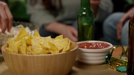 close up of friends at home or in bar drinking alcohol and eating tortilla chips with salsa dip