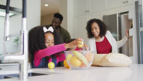 happy african american girl unpacking groceries in kitchen with parents and brother