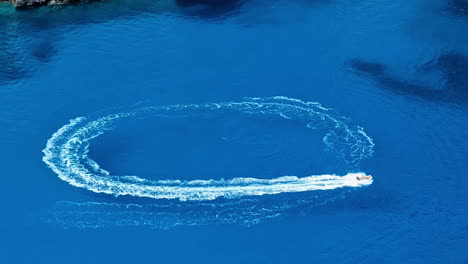 A-motorboat-sails-in-circles-in-the-Blue-Sea-of-Navagio-beach,-Greece,-Aerial