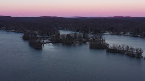 el retroceso de los drones se eleva sobre el lago de invierno en colinas boscosas al atardecer