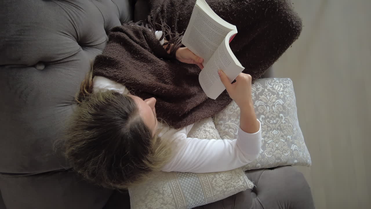 A person enjoys a quiet afternoon reading a book while wrapped in a warm blanket on a soft couch. The serene atmosphere invites relaxation and peace