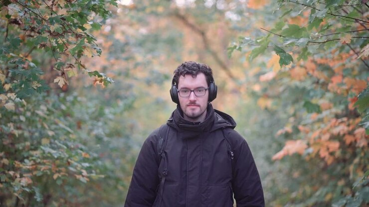 Joyful bearded European man with trendy glasses stands amidst the hues of a mixed autumn forest, radiating happiness and warmth upon seeing viewers, emanating pure positive vibes
