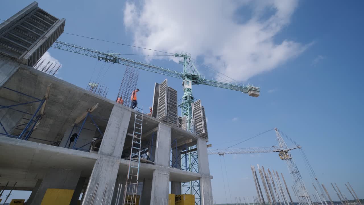 las grúas de torre trabajan en la construcción de edificios residenciales de ladrillo contra el fondo de un cielo azul.