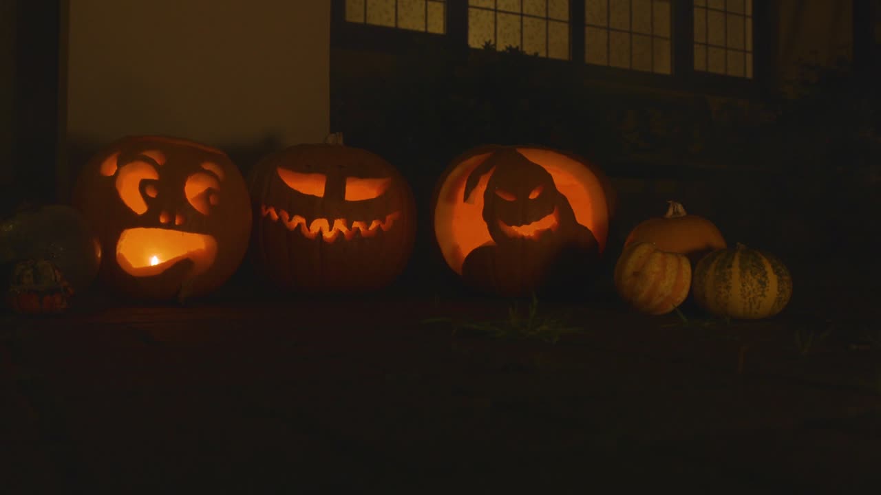 3 carved lit pumpkins outside the front of a house Halloween with small plume of smoke slow motion