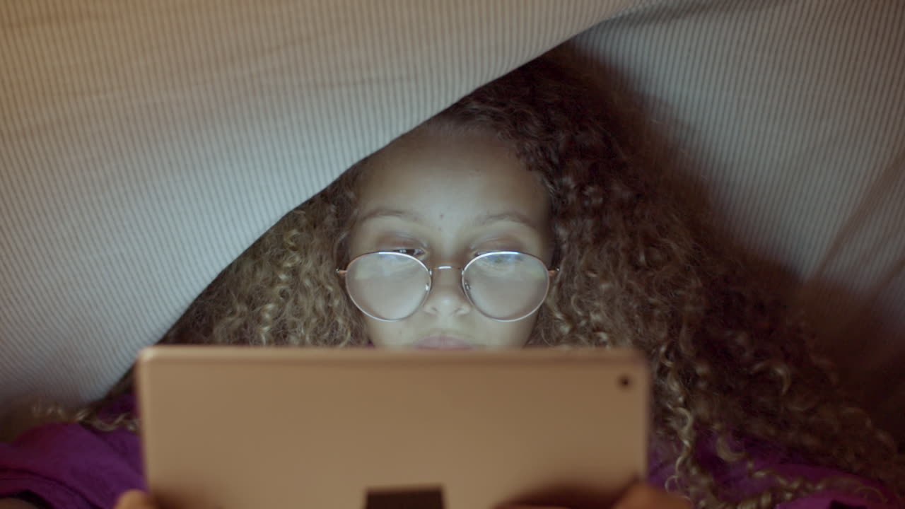 담요 아래에서 전자 책을 읽고 귀여운 소녀의 전면보기 근접 촬영