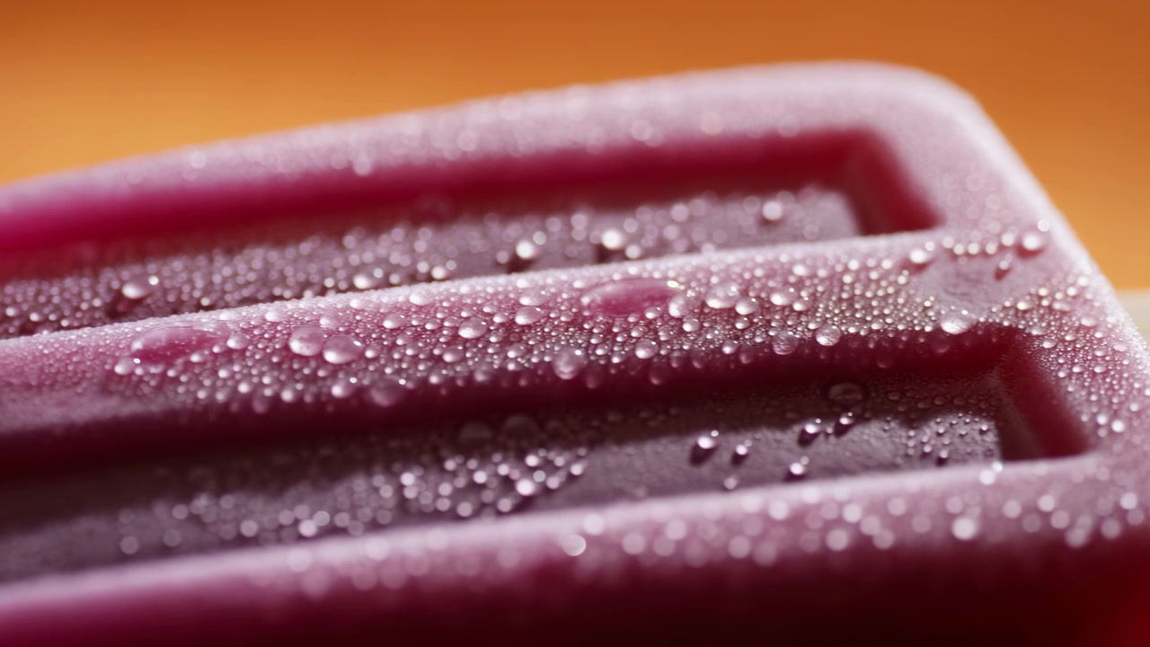 Closeup frozen berry popsicle midsequence with condensation and subtle melting on wooden stick