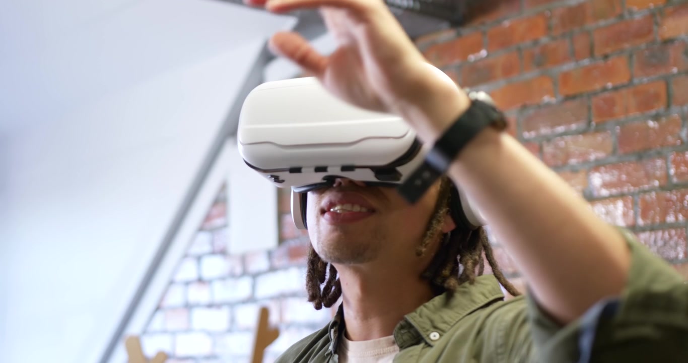 Uomo adulto afroamericano che indossa un visore VR bianco, si protende, tocca ed esplora un loft virtuale