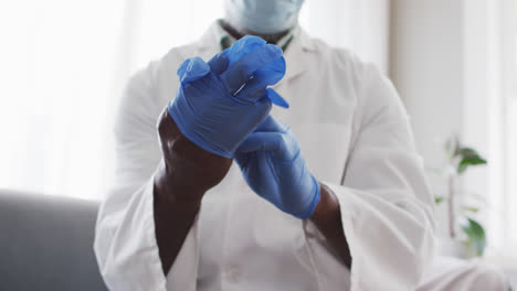 mid section of male african american doctor wearing surgical gloves at home