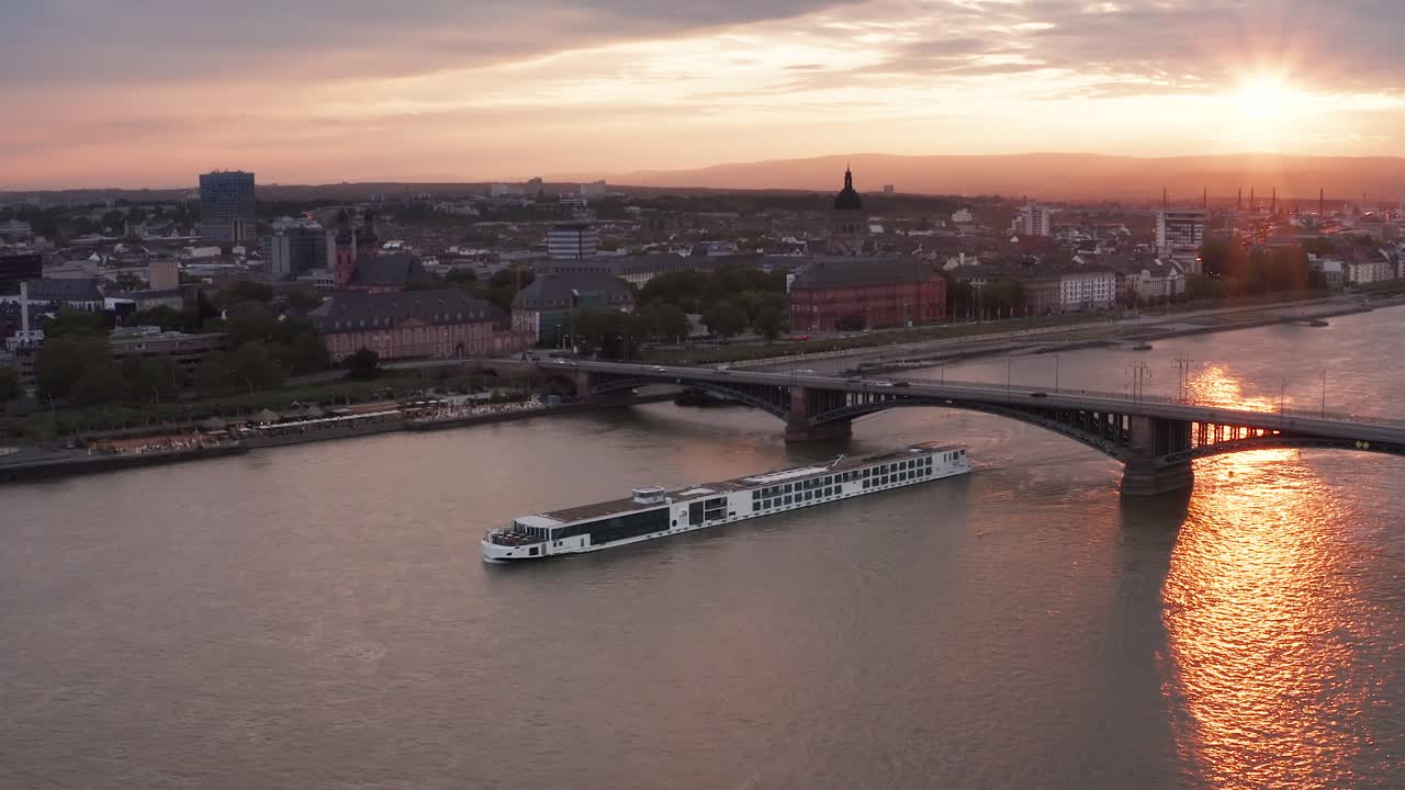 Tramonto rossastro su Magonza in una calda giornata primaverile del 2021, con una nave sul fiume Reno e riflessi del sole sull'acqua.
