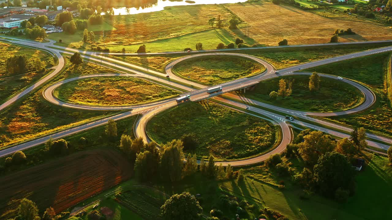 Cloverleaf road interchange in green countryside lit by golden hour light in aerial view