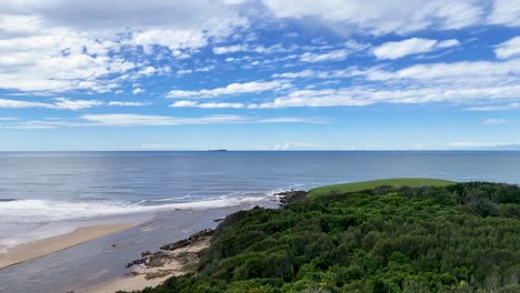 Drone camera smoothly pans across lush headland, sandy beach, and ocean under bright daylight