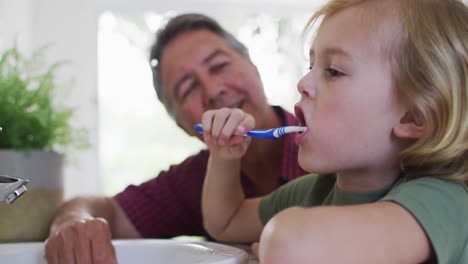 abuelo caucásico ayudando a su nieto a cepillarse los dientes en casa