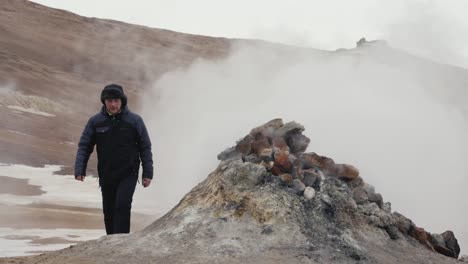 man appear behind of boiling steam vent and continue walking, iceland