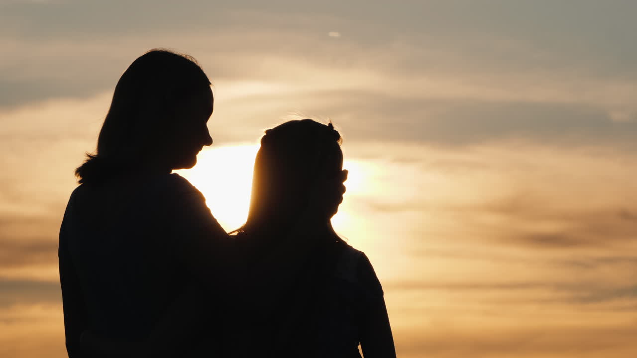 siluetas de mamá e hija contra el cielo y el sol poniente
