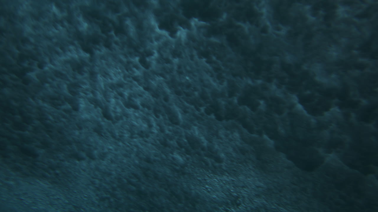 Light glimmers as ocean waves crash breaking on ocean surface in mesmerizing cloud pattern, underwater angle