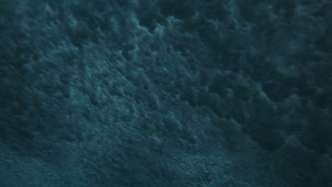 light glimmers as ocean waves crash breaking on ocean surface in mesmerizing cloud pattern, underwater angle