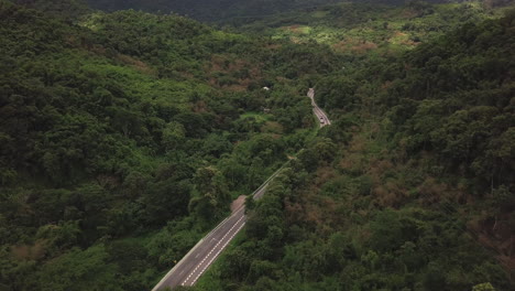 Aerial-view-of-countryside-road-passing-through-the-lush-greenery-and-foliage-tropical-rain-forest-mountain-landscape