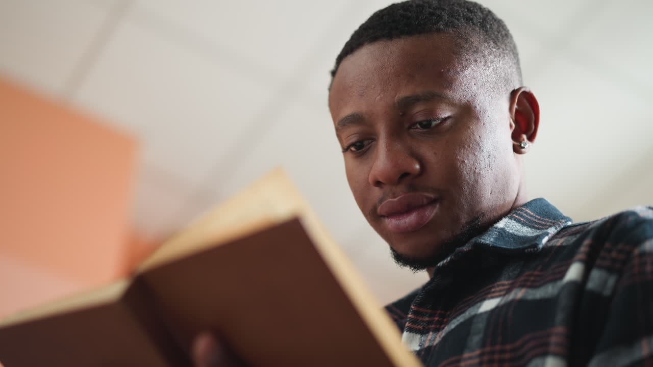 Man reads novel in modern bookstore. African American student focused on studying educational literature in information center. Picking book for home reading