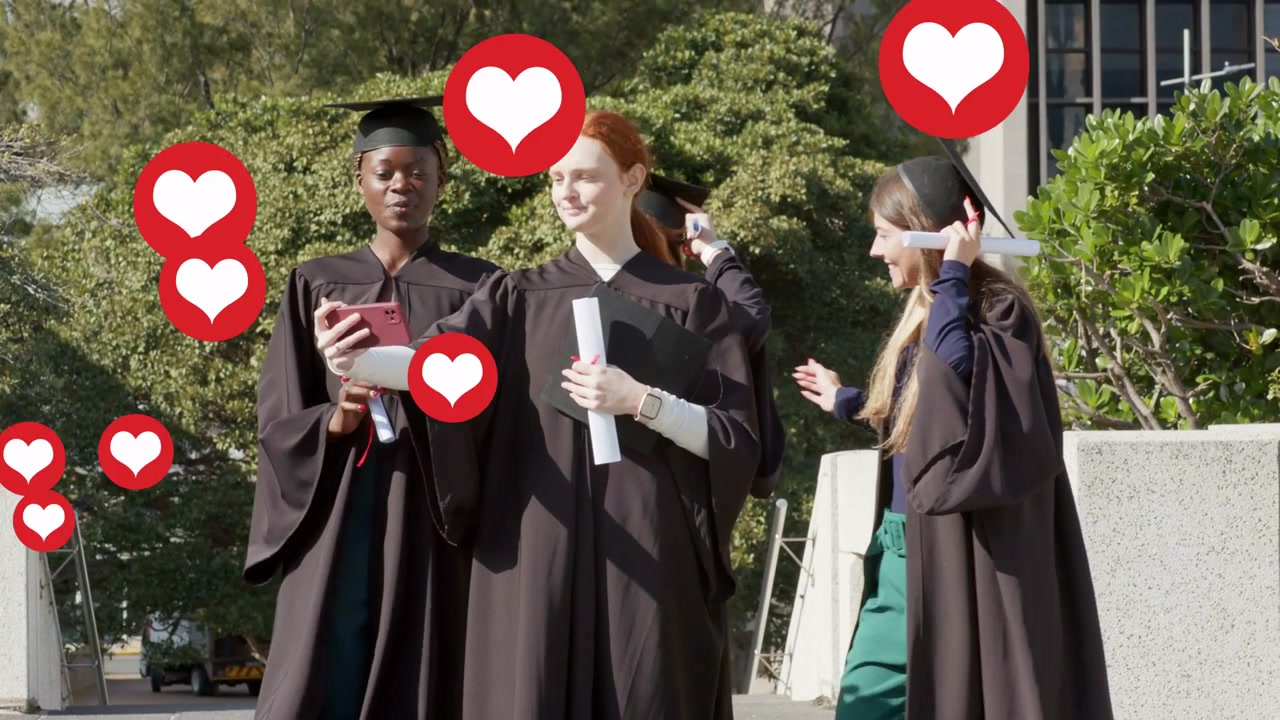 Laureato al centro che alza il telefono per un selfie, amici che si uniscono con i diplomi, cuori rossi che fluttuano per il giorno della laurea