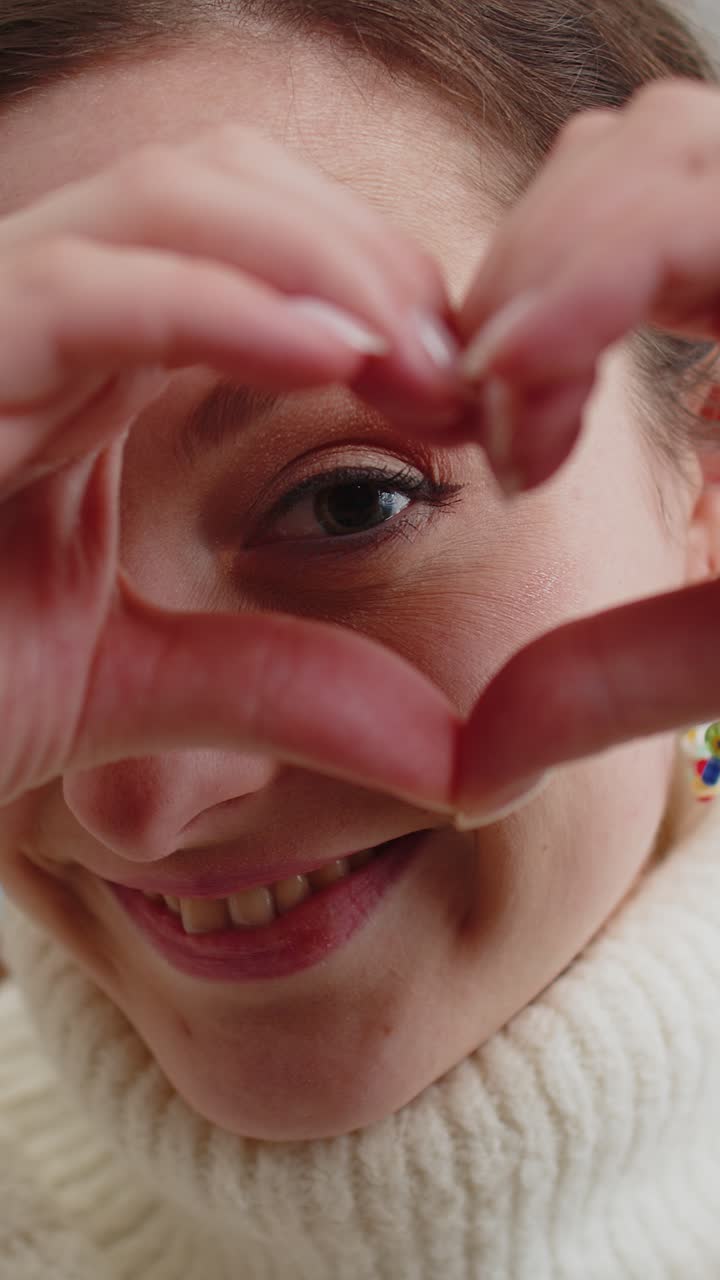 Mulher jovem e feliz faz um símbolo de amor mostrando um sinal de coração para a câmera, expressando sentimentos românticos